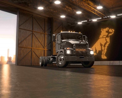 A dark gray electric Mack medium-duty truck in front of a Mack logo.