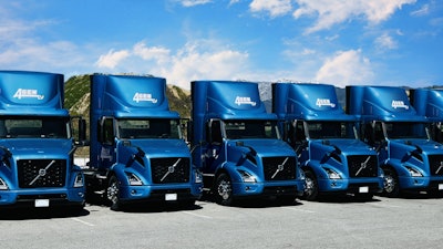 A row of Volvo VNR Electric Trucks parked outside.