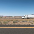 A truck and trailer drives on a highway in the desert.