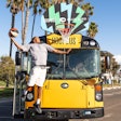 A man dunking a basketball in a hoop attached to an electric school bus from Blue Bird.