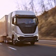 A Nikola Tre semi driving on a highway at sunset.
