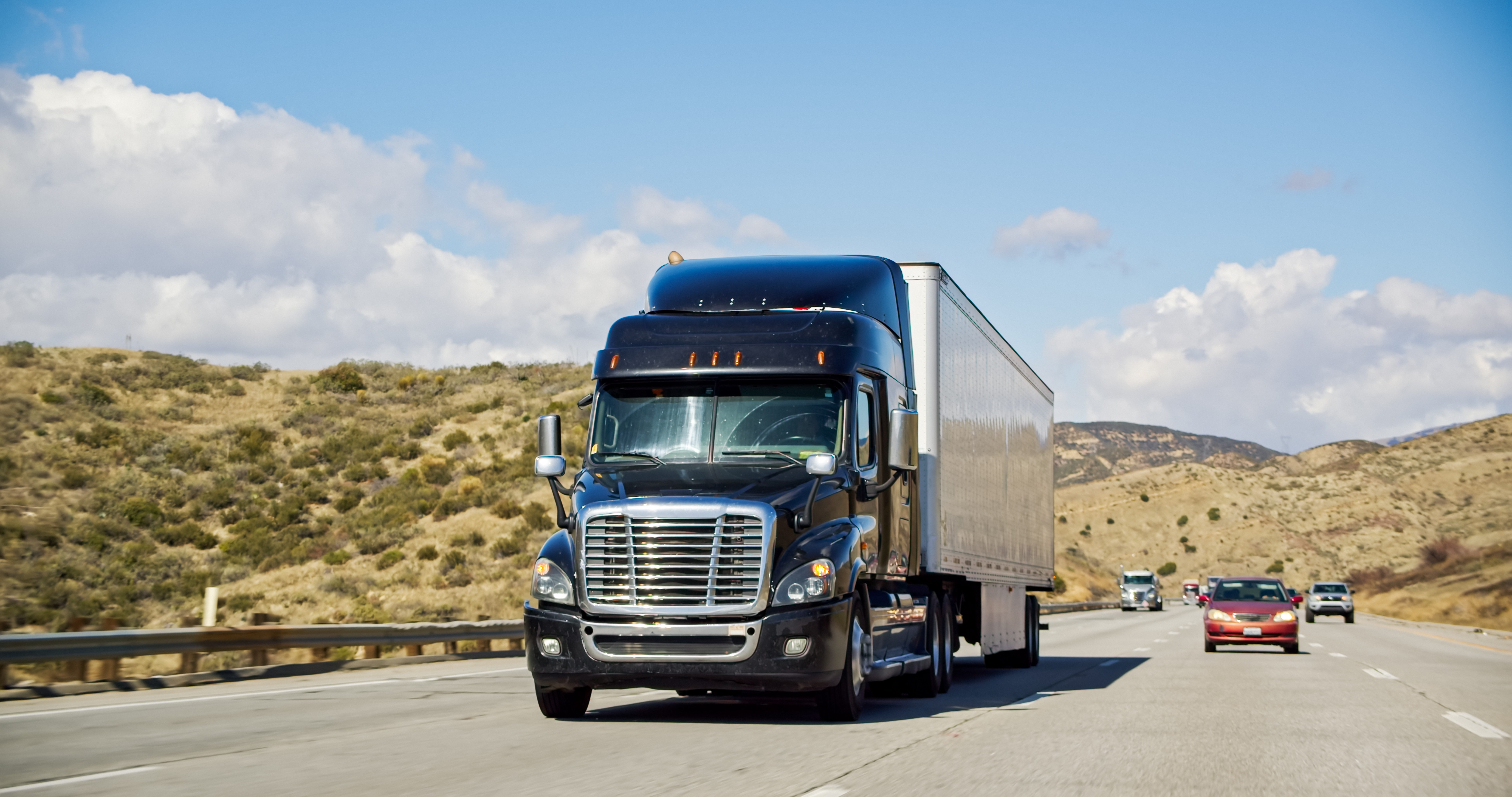 A diesel-powered Class 8 semi truck driving on a Southern California highway.