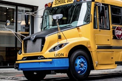 A LION-C battery-electric school bus parked outside a building.