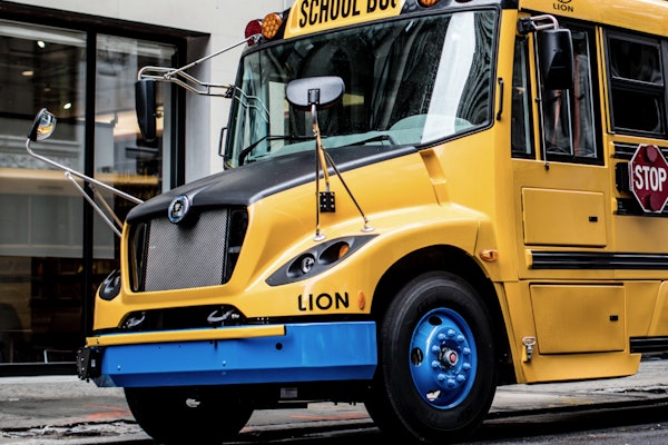 A LION-C battery-electric school bus parked outside a building.