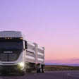 A Nikola Tre Class 8 semi driving on a highway hauling a HYLA-branded hydrogen for refueling payload.