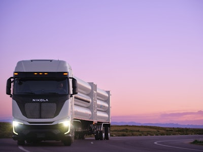 A Nikola Tre Class 8 semi driving on a highway hauling a HYLA-branded hydrogen for refueling payload.