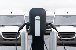 An illustration of small battery-electric commercial vans parked next to a charger.