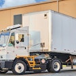 An Orange EV yard tractor hauling a Lazer Logistics trailer at a loading dock.