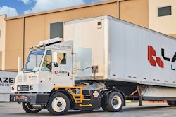 An Orange EV yard tractor hauling a Lazer Logistics trailer at a loading dock.