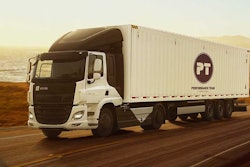 An Einride semi-truck is shown hauling a Performance Team trailer along a beachside highway at sunset.