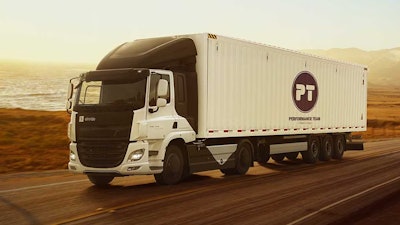 An Einride semi-truck is shown hauling a Performance Team trailer along a beachside highway at sunset.
