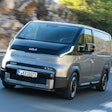 The all-new battery-electric Kia PV5 van driving on a mountain highway.