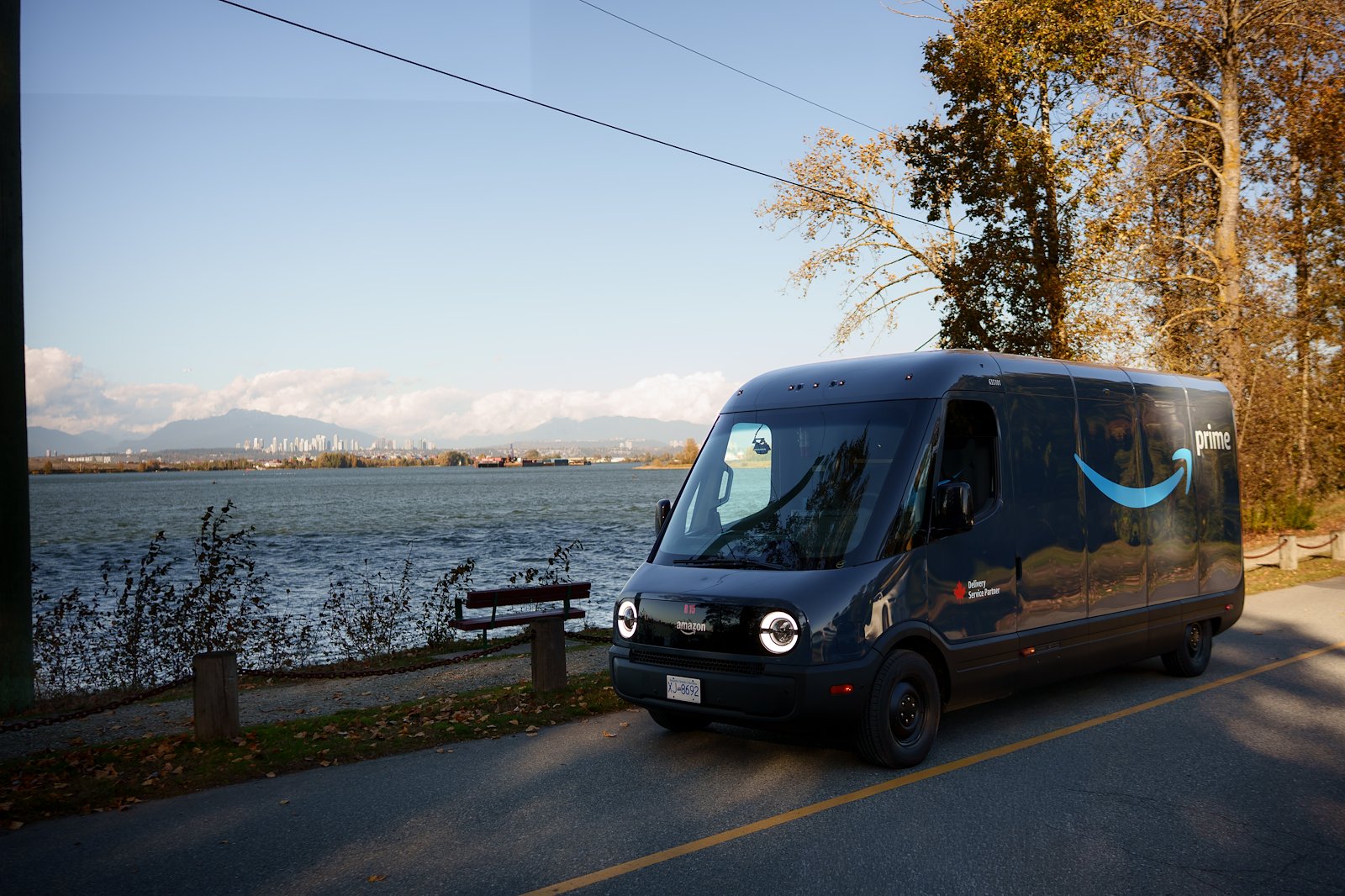 A Rivian Electric Delivery Van operates against the Vancouver skyline as Amazon launches its first EV fleet in Canada.