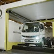 A Mitsubishi Fuso battery-electric truck is shown having its depleted battery replaced with a fully charged one at an Ample battery swapping station, a process which takes about five minutes.