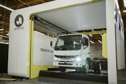 A Mitsubishi Fuso battery-electric truck is shown having its depleted battery replaced with a fully charged one at an Ample battery swapping station, a process which takes about five minutes.