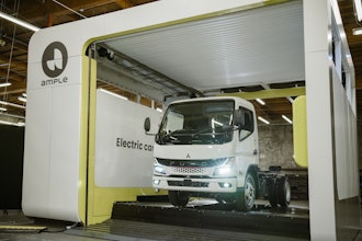 A Mitsubishi Fuso battery-electric truck is shown having its depleted battery replaced with a fully charged one at an Ample battery swapping station, a process which takes about five minutes.