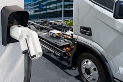An unbranded battery-electric commercial truck is parked next to a charging station, revealing its exposed battery system.