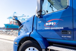 A blue NFI-owned Volvo VNR Electric parked at a shipping port.