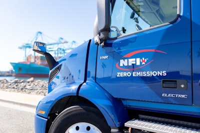 A blue NFI-owned Volvo VNR Electric parked at a shipping port.