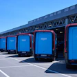Amazon-branded Rivian Electric Delivery Vans lined up at a logistics center.