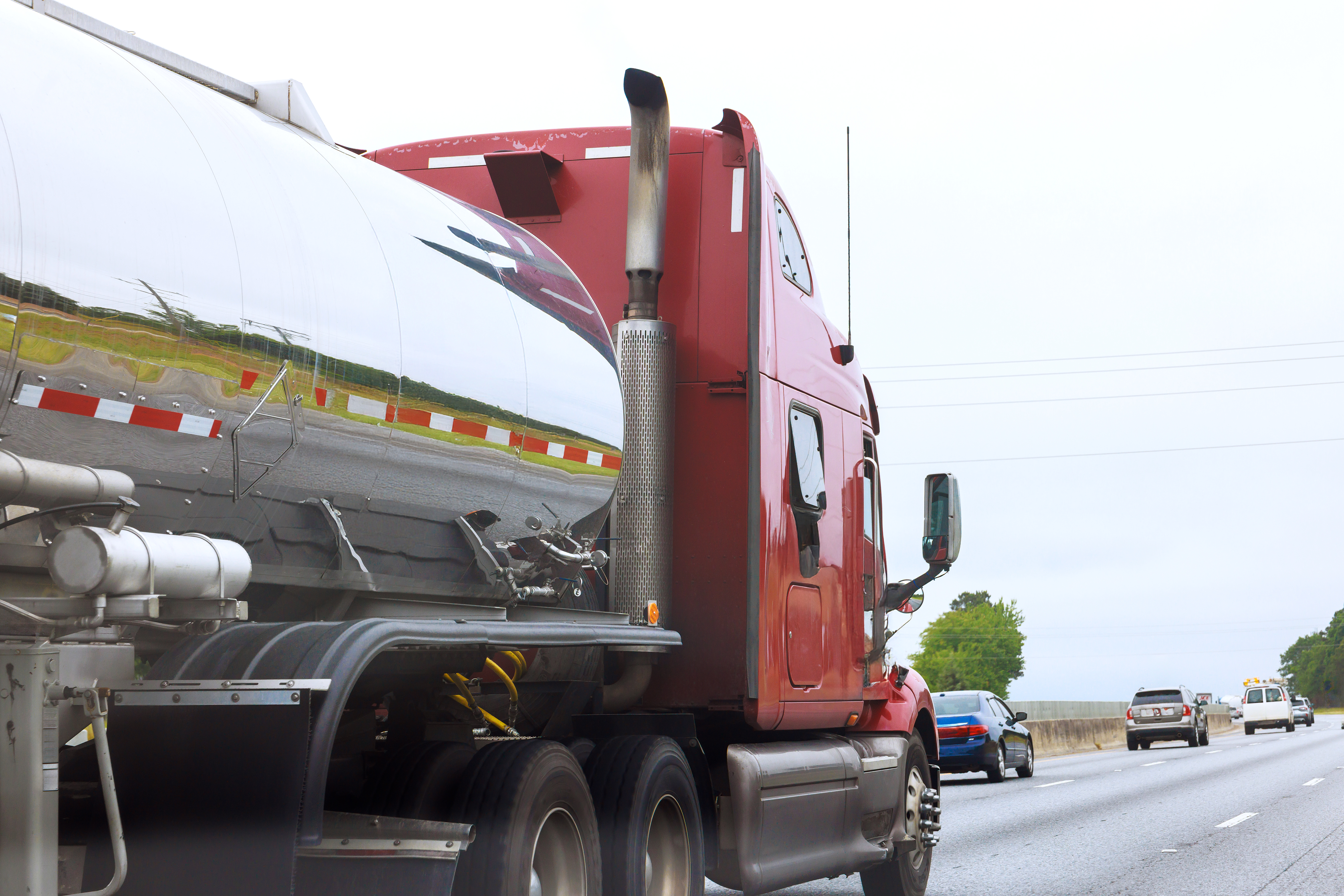 A red semi truck is shown hauling a tanker trailer on a highway.