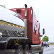 A red semi truck is shown hauling a tanker trailer on a highway.