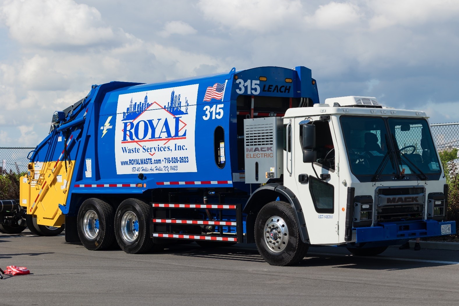 A parked Mack LR Electric garbage truck painted in blue and white Royal Waste Services livery.