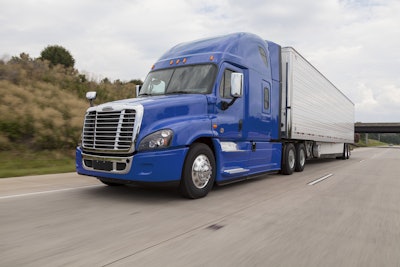 A blue Freightliner Class 8 semi truck hauling a silver trailer driving on a highway.