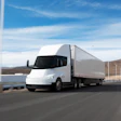 A rendering of a white Tesla Semi pulling a trailer along a scenic coastal highway.