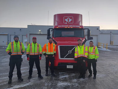 Coke Canada Bottling employees standing in front of a red Volvo VNR Electric.