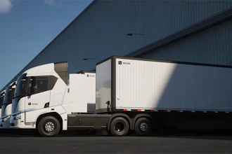 Einride battery-electric semi-trucks parked in front of an industrial warehouse.