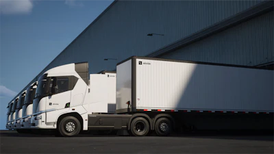 Einride battery-electric semi-trucks parked in front of an industrial warehouse.