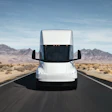 A front-facing view of a white Tesla Semi driving along a desert highway.