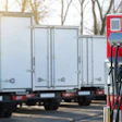 An electric vehicle charging station with multiple cables in an outdoor parking lot, with battery-electric-powered trucks in the background.