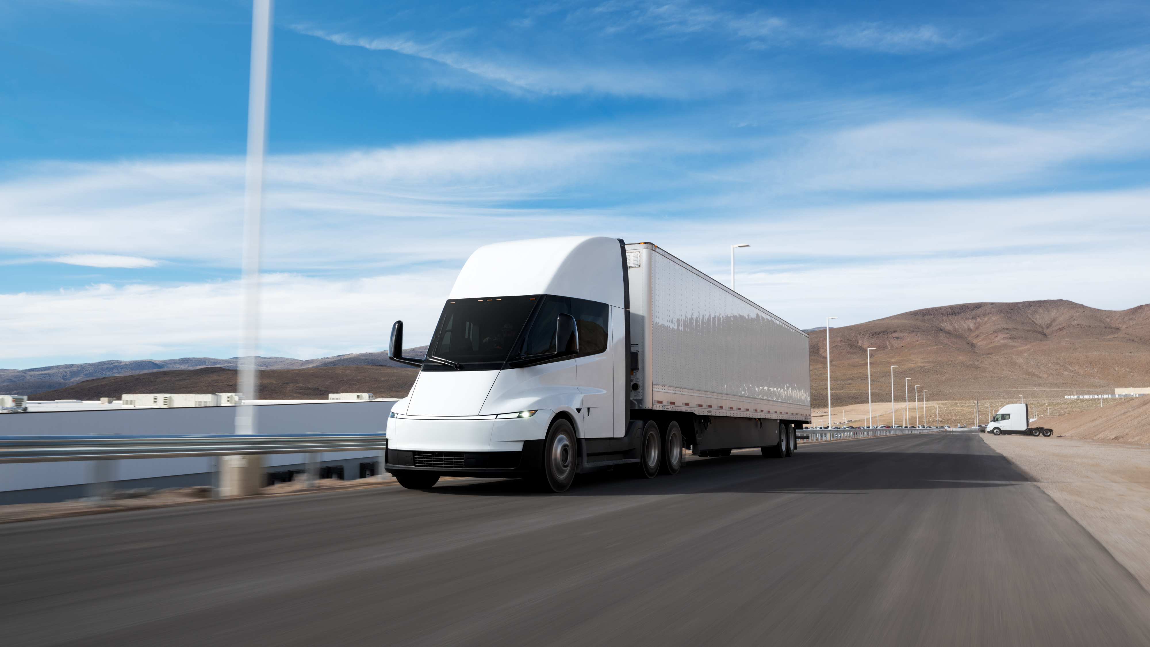 A white Tesla Semi hauling a trailer driving along a coastal road.