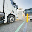 A pair of battery-electric commercial trucks charging at an unknown location.
