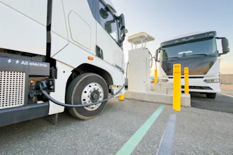 A pair of battery-electric commercial trucks charging at an unknown location.