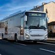 A natural gas-powered IVECO BUS passenger bus travels along an urban street.