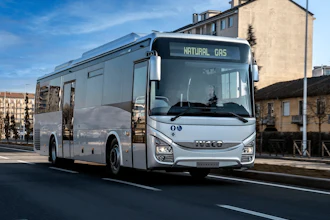 A natural gas-powered IVECO BUS passenger bus travels along an urban street.