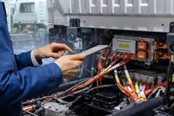 A technician holding a digital tablet next to an electric truck.