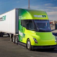A green and yellow WattEV branded Tesla Semi and trailer parked at an industrial facility.